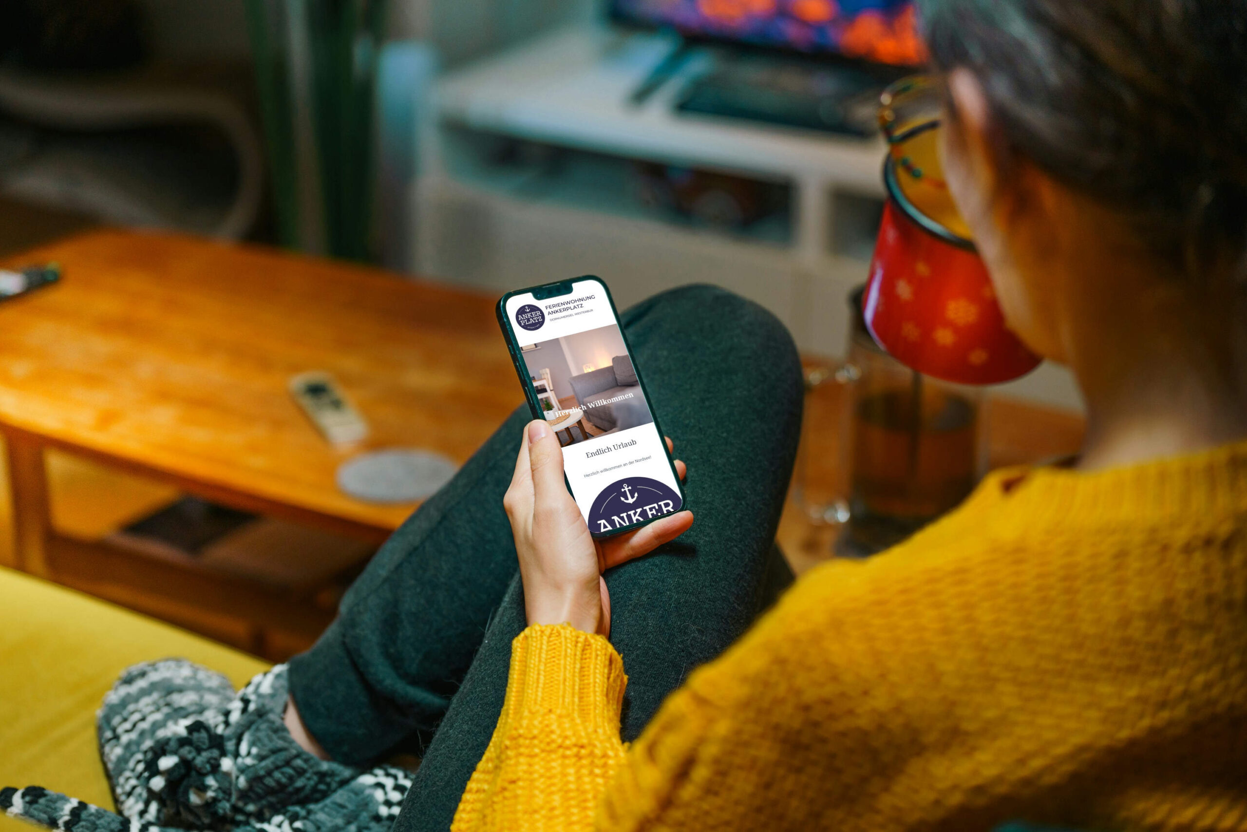 Eine Frau sitzt auf dem Sofa und liest eine digitale Gästemappe der Ferienwohnung Ankerplatz auf ihrem Smartphone